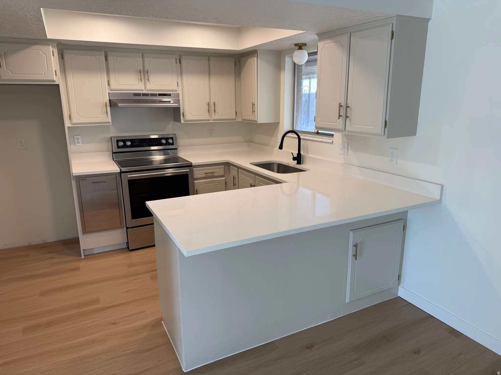 Kitchen featuring light cabinetry, solid surface countertops, stainless steel appliances, a stainless steel sink, and wood-finish flooring