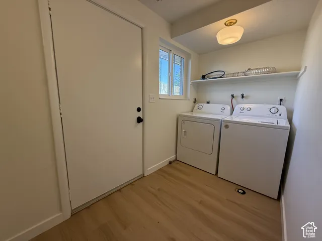 Laundry area with a white door, a window with horizontal panes, wood-finish flooring, a white wall-mounted shelf, and a ceiling-mounted light fixture