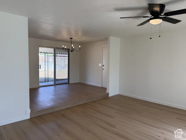 Wood-finish flooring throughout, sliding glass door with screen, multi-light chandelier, and ceiling fan with integrated lighting