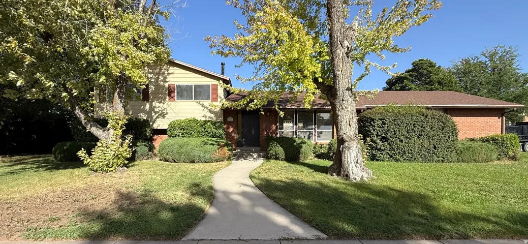 Established landscaping with mature trees, a curving concrete pathway, and a two-story section with red shutters