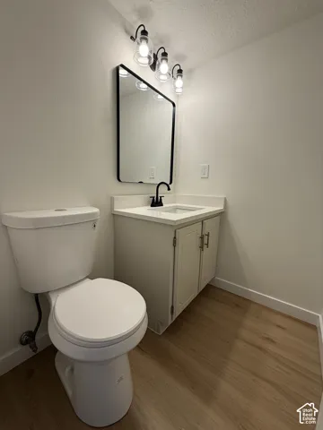 White vanity with countertop, framed mirror, black fixtures, and wood-finish flooring