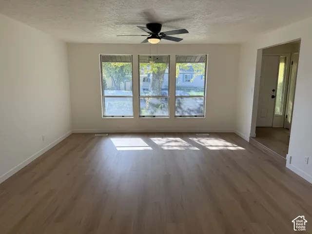 Spacious room with wood-finish flooring, three large windows, a ceiling fan, and light-toned walls