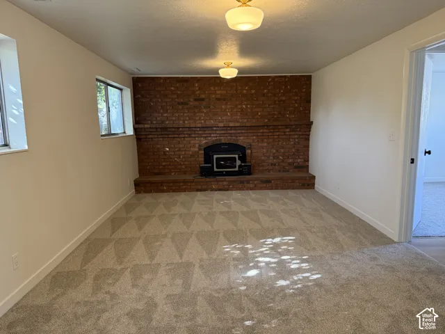 Brick accent wall with a built-in fireplace, two windows, two flush-mount ceiling lights, and patterned carpet flooring