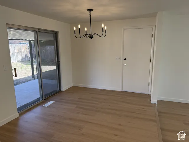 Wood-finish flooring, sliding glass door, patio with concrete surface, black chandelier, and white interior walls