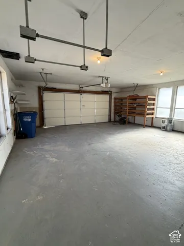 Attached garage with an overhead door, concrete flooring, built-in shelving, and multiple windows