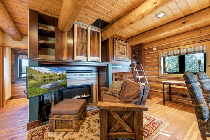Wood-planked ceiling with exposed log beams, log wall construction, built-in cabinetry, and a fireplace with a wood mantel