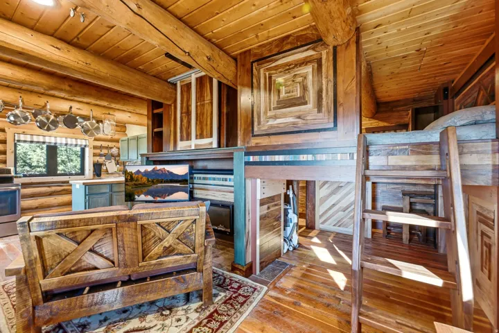 Log cabin interior with exposed wood beams, wood-finish flooring, and a built-in bunk bed with ladder