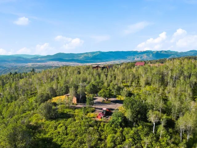 Mountain backdrop, verdant landscape, mature trees, single-story structure, expansive acreage
