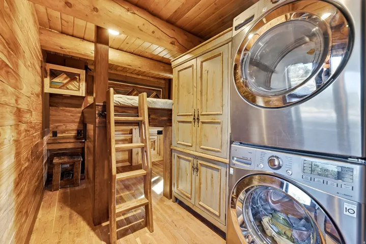 Stacked washer and dryer, wood-finish flooring, wood-paneled walls, built-in cabinetry, and wood beam ceiling