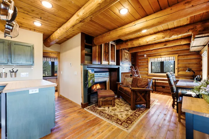 Exposed log walls and ceiling beams, wood-plank flooring, fireplace with mantel, built-in shelving, and recessed lighting