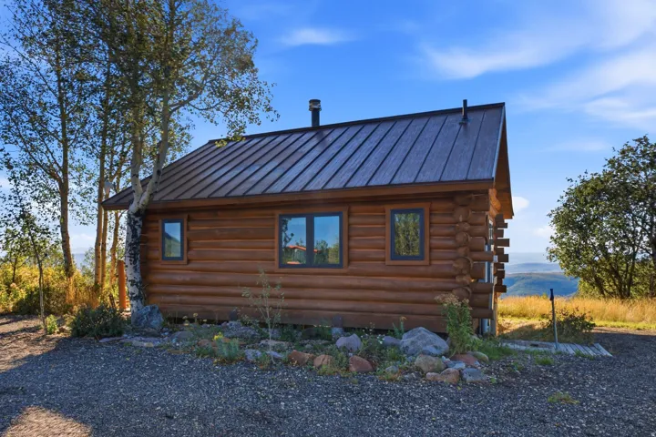 Log cabin exterior with a dark metal roof, multiple windows, and a gravel perimeter