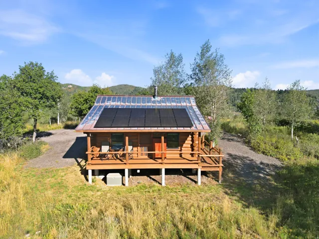 Log cabin structure with an elevated wooden deck, featuring a metal roof with integrated solar panels