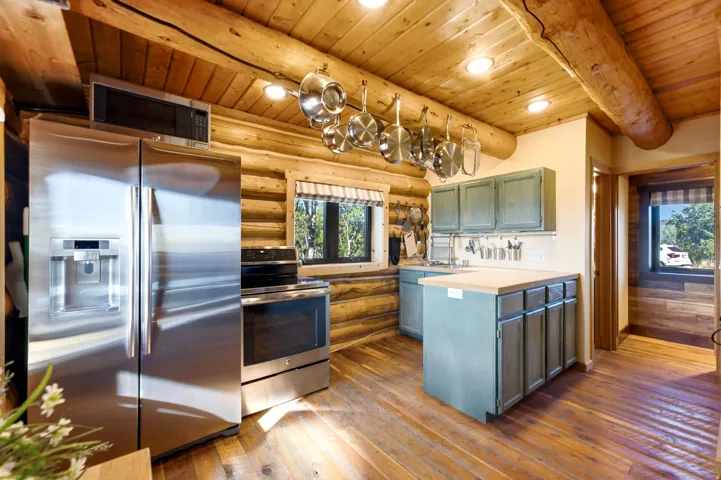 Kitchen featuring wood-finish flooring, exposed log walls, stainless steel appliances, distressed blue cabinetry, and overhead lighting