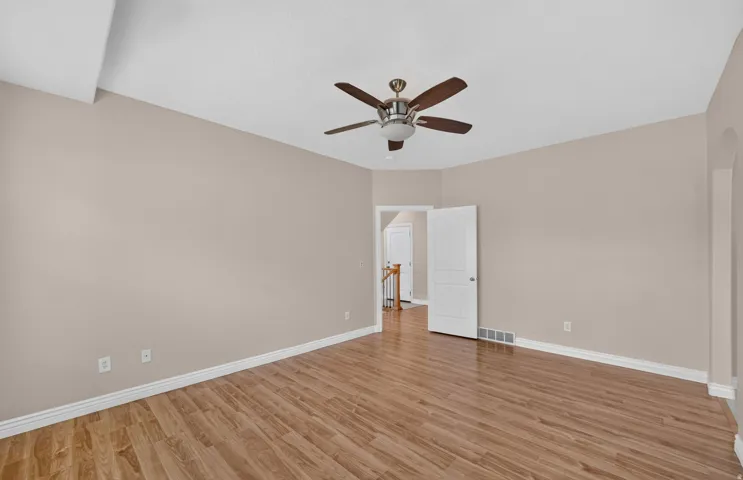 Wood-finish flooring, ceiling fan with integrated lighting, neutral wall tones, and an arched entry