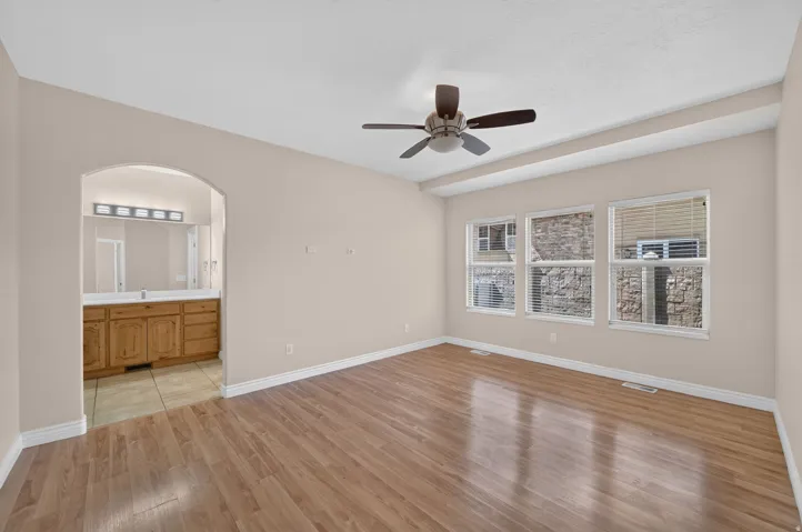 Spacious room featuring wood-finish flooring, ceiling fan, and a wall of three windows