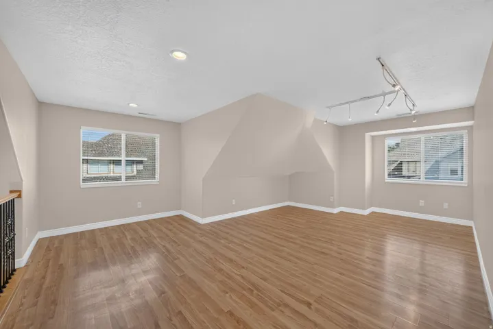 Spacious room featuring wood-finish flooring, two windows with blinds, recessed lighting, and track lighting