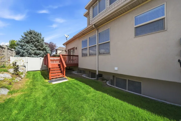 Expansive backyard with a manicured lawn, a wooden deck with stairs, a white privacy fence, and mature landscaping
