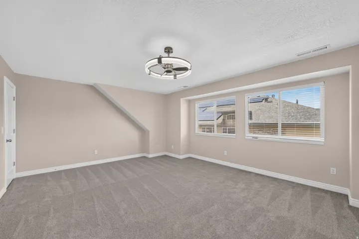 Spacious room with gray carpeting, two windows, and a modern ceiling fan with integrated lighting