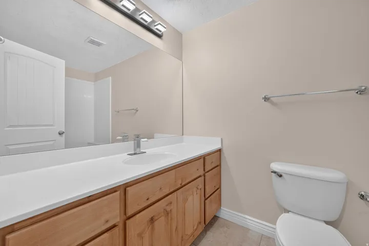 Bathroom featuring a wood-finish vanity with a white countertop and integrated sink, a large wall-mounted mirror, and tile flooring