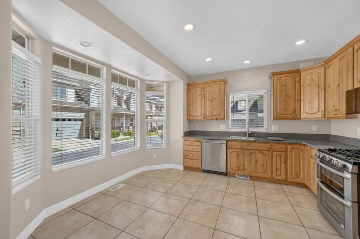 Kitchen featuring tile flooring, wood-finish cabinetry, stainless steel appliances, and a bay window