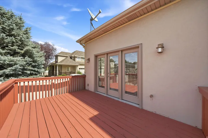 Expansive wood-finish deck with railing, triple glass panel doors, and stucco exterior