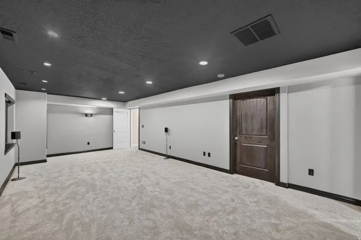 Recessed lighting illuminates the expansive carpeted area with a dark ceiling