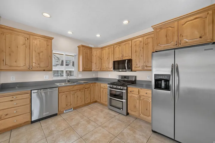 Kitchen with light wood cabinetry, stainless steel appliances, grey countertops, and recessed lighting