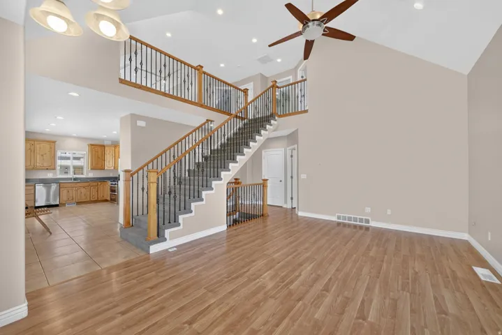 Two-story ceiling, wood-finish flooring, staircase with wrought iron balusters, recessed lighting, and a ceiling fan