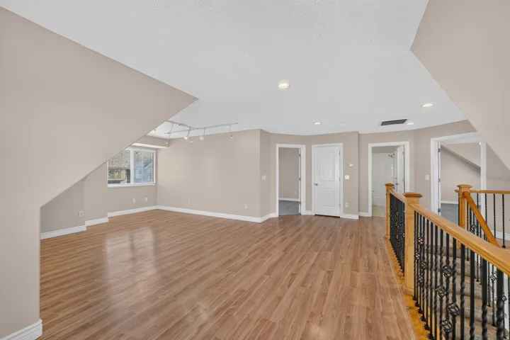 Spacious room featuring wood-finish flooring, neutral wall tones, track lighting, and multiple window openings