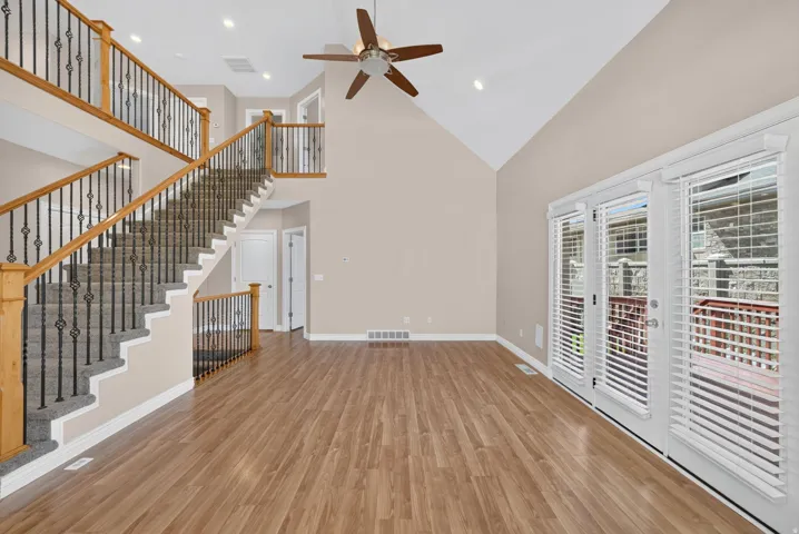 Vaulted ceiling with a ceiling fan, wood-finish flooring, two-story staircase with wrought iron balusters, recessed lighting, and French doors