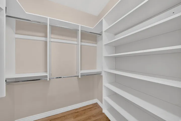 Walk-in closet with built-in shelving, hanging rods, and wood-finish flooring