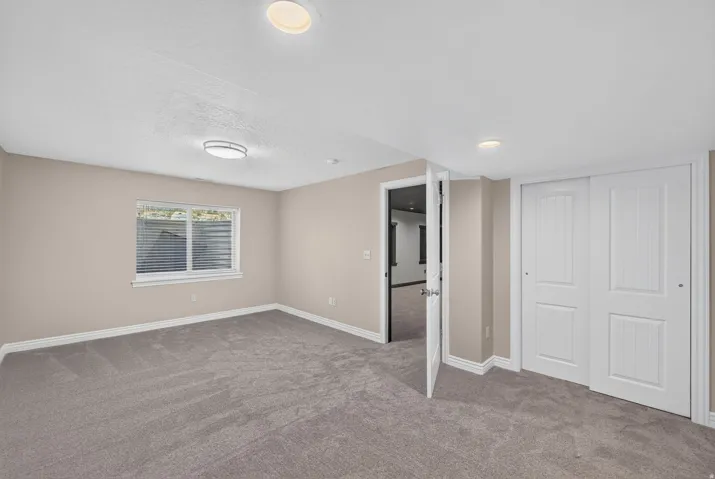 Neutral-toned walls, gray carpeting, recessed ceiling lighting, a window with horizontal blinds, and a sliding panel door closet