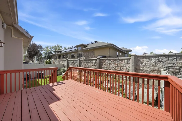 Spacious wood deck with railing and stairs, overlooking a landscaped yard with a stone-finish retaining wall