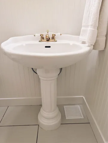 White pedestal sink with a brass-finish faucet.