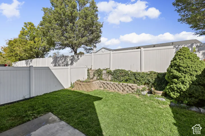 Expansive backyard featuring a manicured lawn, white privacy fencing, and a tiered retaining wall with integrated plantings