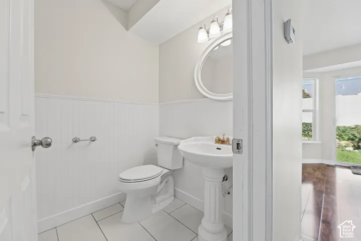 Pedestal sink, white beadboard paneling, tiled flooring, round framed mirror, and a three-light vanity fixture
