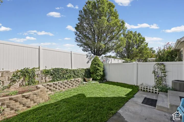 Manicured lawn area with a concrete patio, retaining walls with lush plantings, and a privacy fence