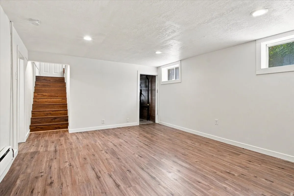 Spacious room featuring wood-finish flooring, white walls, recessed lighting, two windows, and a wooden staircase