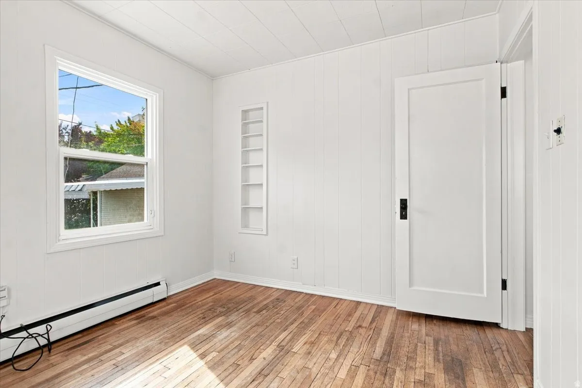 Wood-finish flooring, white paneled walls, a single-hung window, built-in shelving, and a solid core door with black hardware