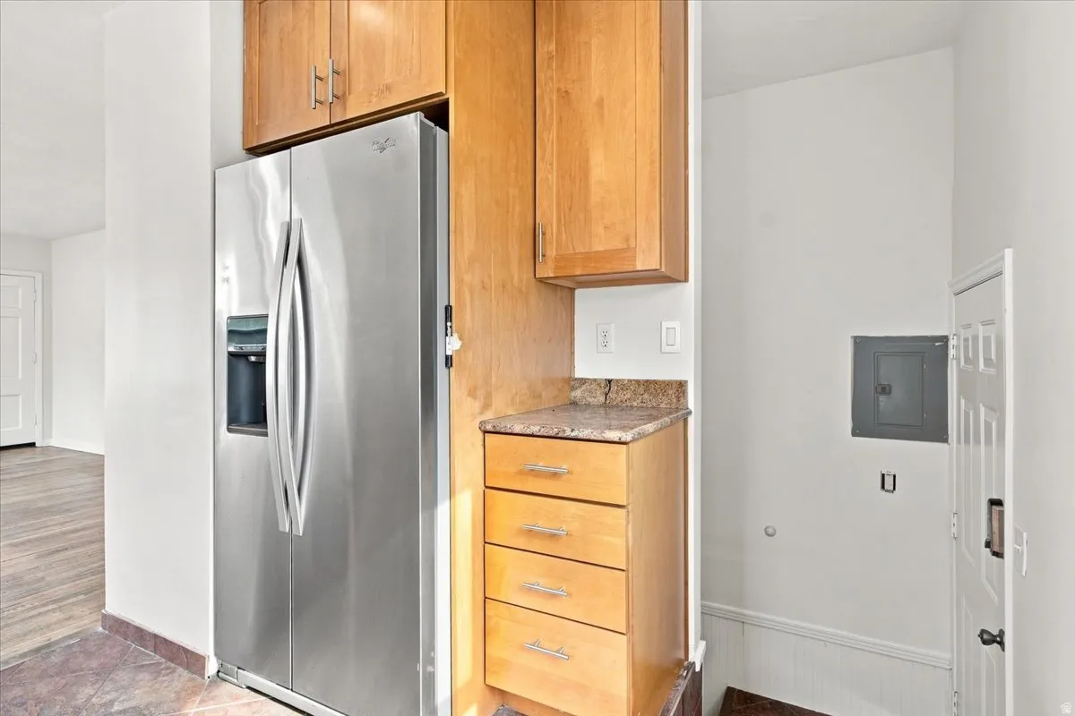 Stainless steel refrigerator with ice and water dispenser, light wood cabinetry, stone countertop, and wood-finish flooring