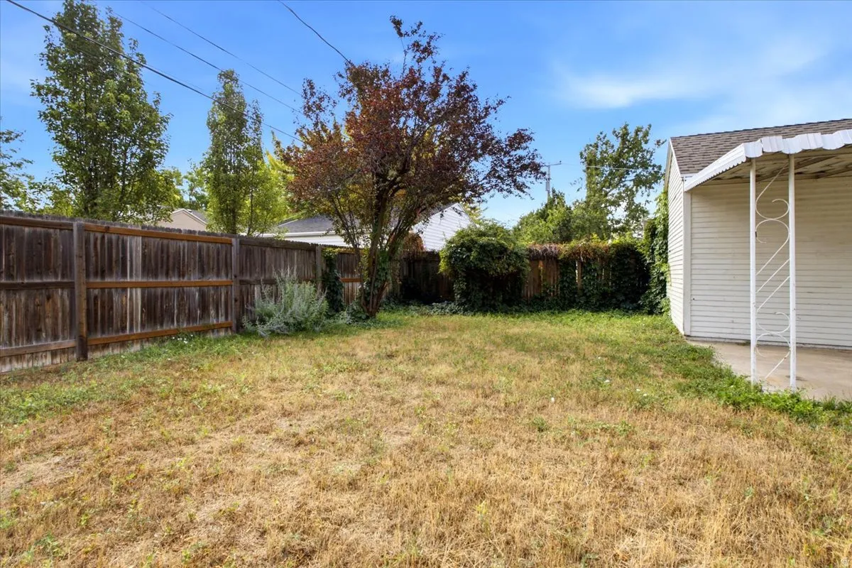Expansive backyard featuring a wood privacy fence, mature trees, and a covered porch with decorative metal supports