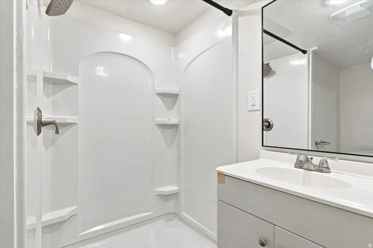 White shower stall with built-in shelving, brushed nickel showerhead, and a coordinating vanity with a basin sink and dual-handle faucet