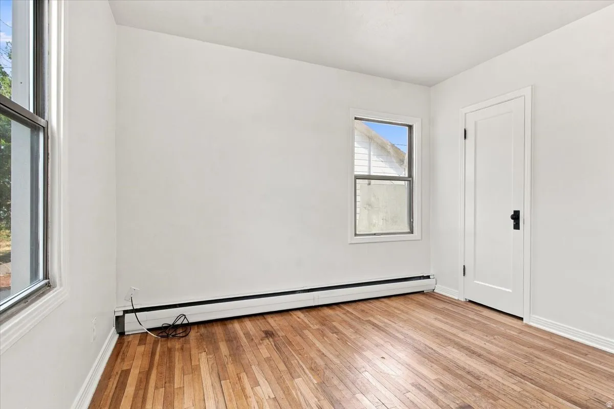 Hardwood flooring, white painted walls, white trim, white door with black hardware, and two windows