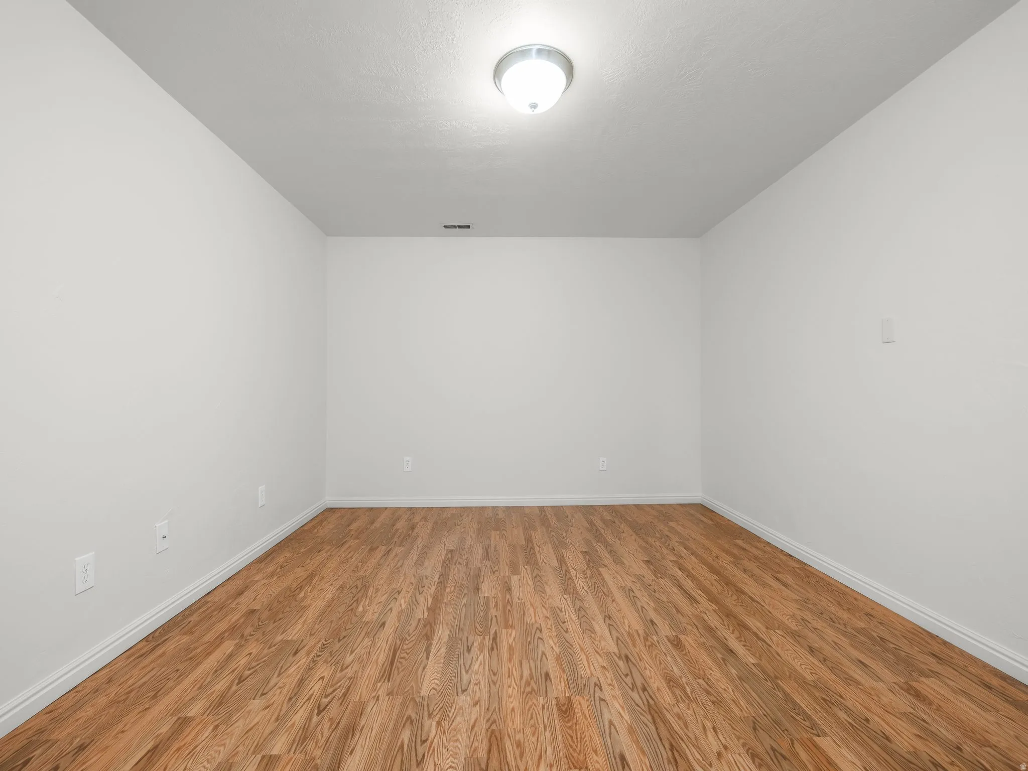 Wood-finish flooring with white baseboards, bright walls, and a ceiling-mounted light fixture