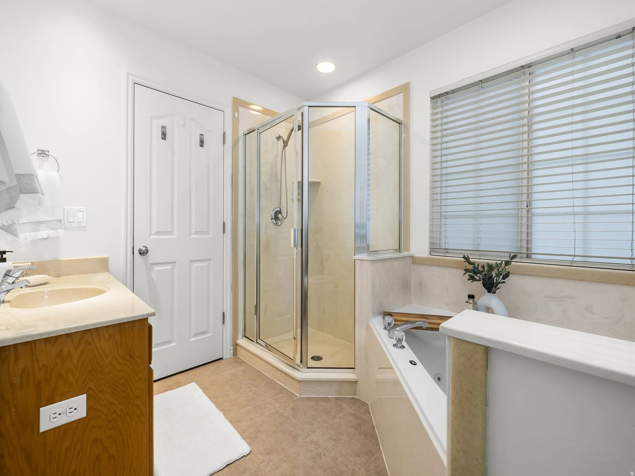 Primary bathroom, with glass-enclosed shower, built-in soaking tub, vanity with integrated sink, wood-finish cabinetry, and tiled flooring