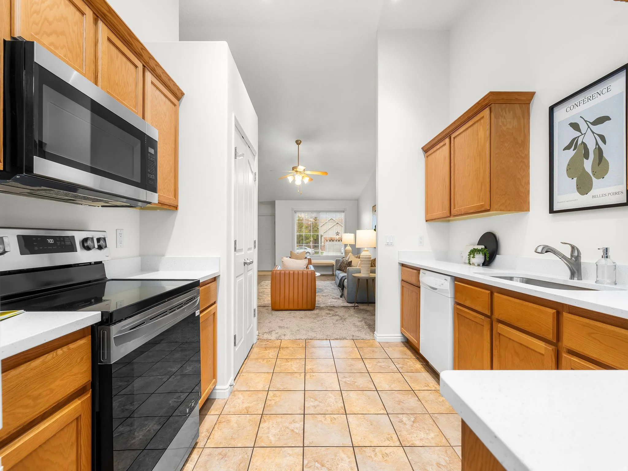 Kitchen featuring wood-finish cabinetry, stainless steel appliances including a built-in microwave and electric range, white countertops, and terra cotta tile flooring