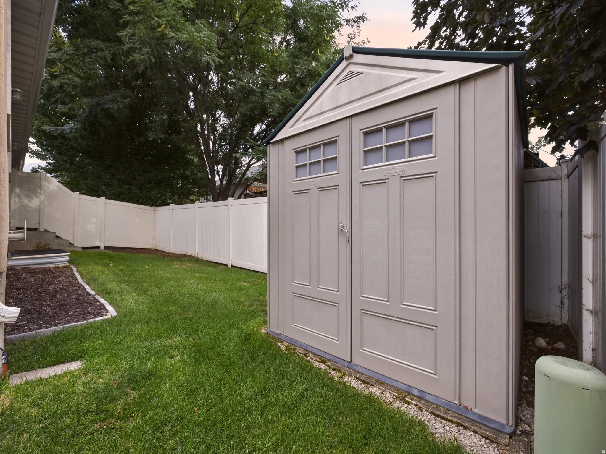 Fenced backyard with a storage shed, featuring a gabled roof and double doors with transom windows