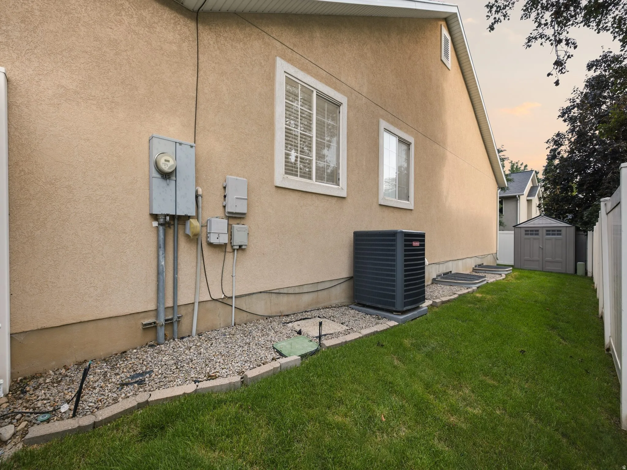 Beige stucco exterior with white-framed windows, a gray shed, and a white privacy fence