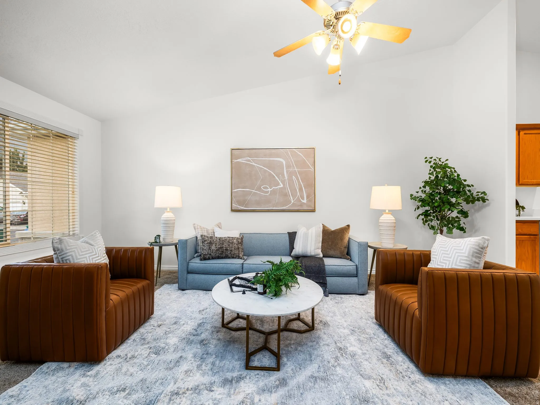 Sophisticated living room showcasing a blue upholstered sofa, cognac leather barrel chairs with vertical ribbed detailing, and a round marble-top cocktail table with geometric metal base
