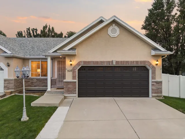 Stucco exterior with brick accents, attached dark garage door, concrete driveway, and a manicured lawn